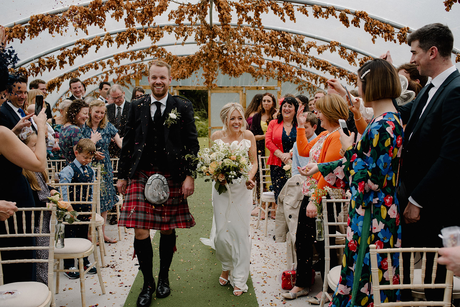 Emma and Dan walking down the aisle in the polytunnel at Colstoun.