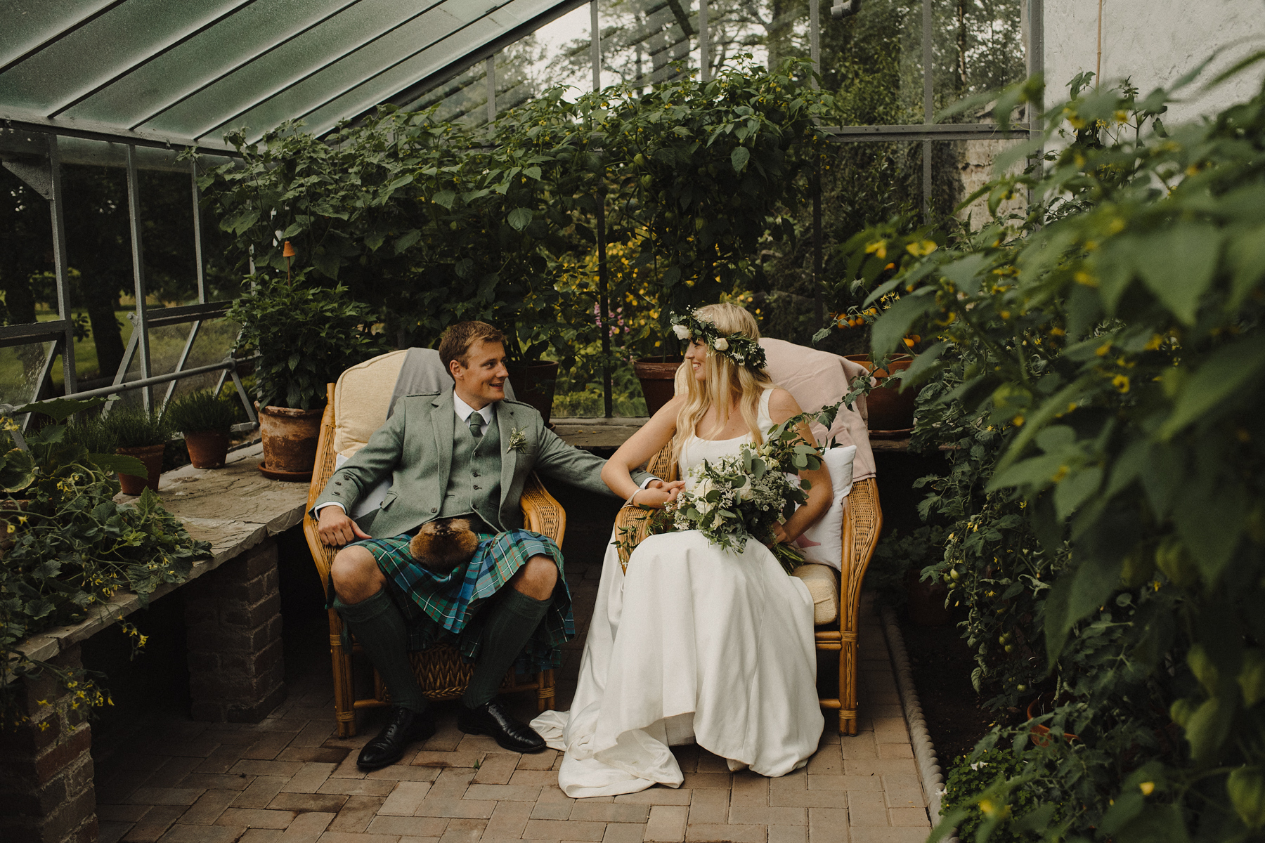 Wedding photo of bride in groom sitting on chairs in the greenhouse.