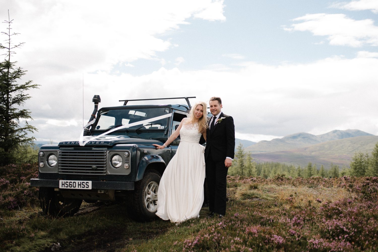 Wedding couple standing next to Range Rover after getting married on top of the mountain in Scotland. 